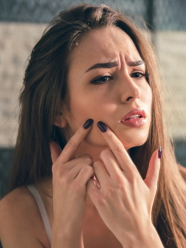 Beautiful girl in white bra is squeezing acne on her face while looking into the mirror in bathroom
