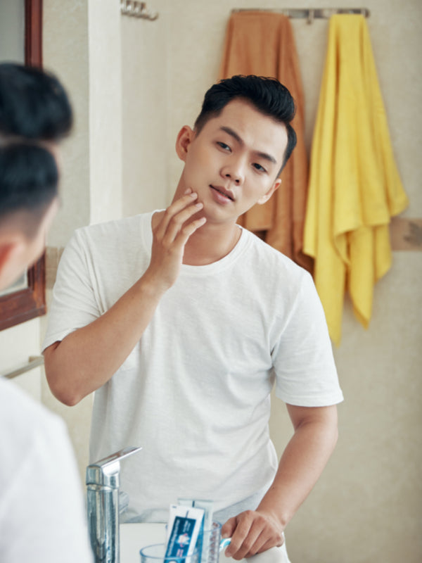 Young man examining his facial skin in the bathroom mirror